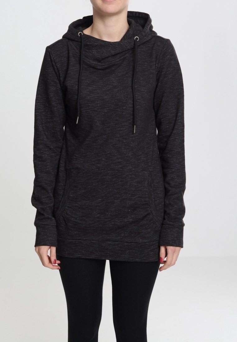 Personne portant un sweat à capuche gris foncé à manches longues avec une poche sur le devant et un legging noir sur un fond uni.
