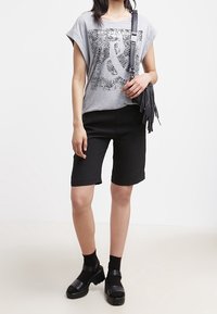 Harmaa lyhythihainen T-paita, jossa on seeprahkuvio ja "&" grafiikka, yhdistettynä mustiin polviin saakka ulottuviin shortseihin ja platform-kengiin. Musta olkalaukku, jossa on tupsut.