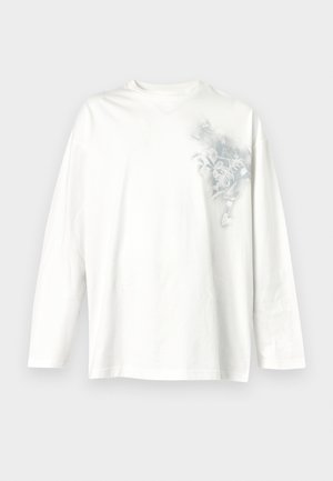 T-shirt blanc à manches longues avec col rond et un motif floral gris subtil sur la partie supérieure gauche de la poitrine.