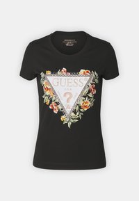 T-shirt noir avec un graphique triangulaire agrémenté de motifs floraux dans des couleurs telles que le rose et le vert, et le nom de la marque "GUESS" en blanc.