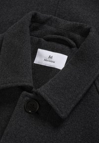 Cappotto in lana grigio scuro con colletto a revenche, chiusura con un bottone e un'etichetta interna. Texture morbida e design minimal.