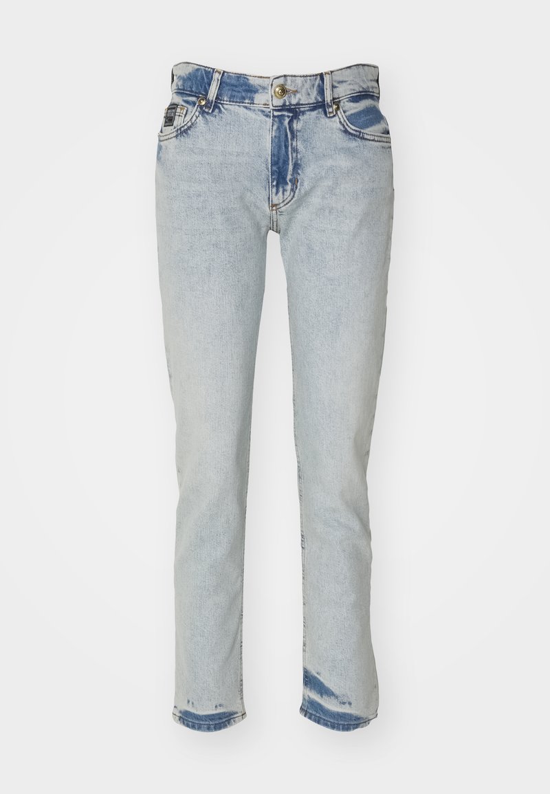 Jasnoniebieskie dżinsy z efektem przecierania, z guzikowym zapięciem i pięcioma kieszeniami. Zniszczone łatki w ciemniejszym niebieskim kolorze na biodrach i u dołu.