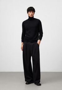 Czarny sweter z kołnierzem typu turtle neck o dopasowanym kroju, w połączeniu z luźnymi, szerokimi spodniami czarnymi. Gładka faktura materiału i minimalne detale na całej powierzchni.