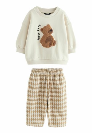 Sweatshirt crème avec un appliqué en forme d'ours en peluche marron et le texte "SUPER CUTE" ; short beige avec un motif en losanges et une taille élastique.