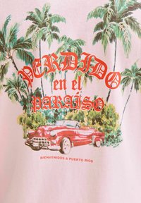 Rozā t-krekls ar tropisko palmu koku grafiku un vintage sarkano kabrioletu, ar uzrakstiem "Perdido en el Paraíso" un "Bienvenidos a Puerto Rico."