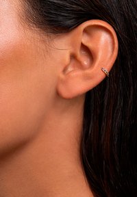 Orecchino a cerchio dorato con tre piccole gemme viola, che abbracciano il lobo dell'orecchio. Pelle chiara e capelli scuri e lisci incorniciano parzialmente l'orecchio.