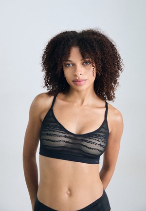 Zwarte kant bralette met doorzichtige bovenlaag, verstelbare bandjes en een naadloze band. Heeft een zachte textuur en een gelaagd golvend patroon.