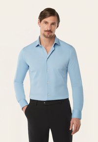 Lichtblauw overhemd met lange mouwen en een-button down kraag, voorzien van doorzichtige knopen en een gladde textuur, gecombineerd met zwarte broek.