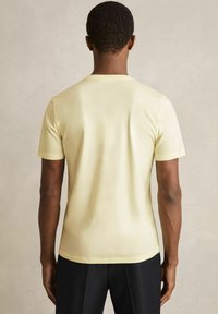 Tricou cu mânecă scurtă și guler rotund, din bumbac galben deschis. Prezintă o formă ajustată, cu o textură netedă și un design minimalistic.