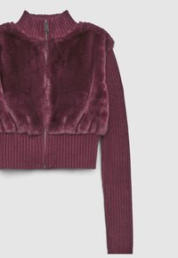 Maglione corto bordeaux con texture a coste; presenta un pannello in pelliccia sintetica sulle spalle e un colletto alto con chiusura a zip.