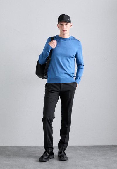 Šviesiai mėlynas megztinis su apvaliu kaklu, juodos kelnės ir juodi batai. Išvaizdą užbaigia juodas kepurė ir kuprinė.