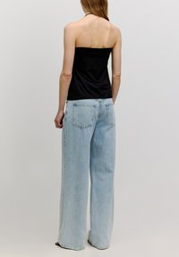 Schwarzes trägerloses Top mit enganliegendem Oberteil, kombiniert mit hellblauen weiten Jeans. Die Jeans verfügen über ein klassisches Fünf-Taschen-Design.