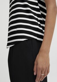 Top de manga corta a rayas en blanco y negro con cuello redondo, combinado con pantalones negros. Tejido suave con un ajuste relajado.