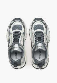 Jasnoszare i czarne buty sportowe, z przewiewną siateczkową cholewką, teksturowanymi akcentami, grubymi amortyzującymi podeszwami oraz kontrastowymi sznurowadłami.