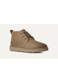 Botas de ante marrón hasta el tobillo con cordones, con puntera redonda, detalles de costura y suela de goma con un patrón de agarre texturizado.
