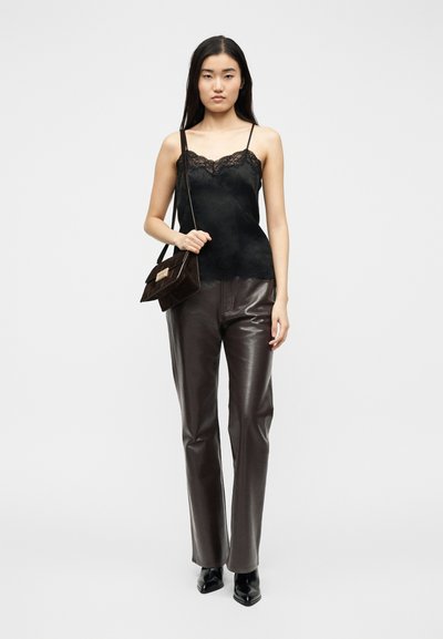 Ženska, ki nosi črno majico s  čipkastim robom, temno rjave usnjene hlače, črne ostro koničaste škornje in drži usklajeno rjavo torbico čez ramo.