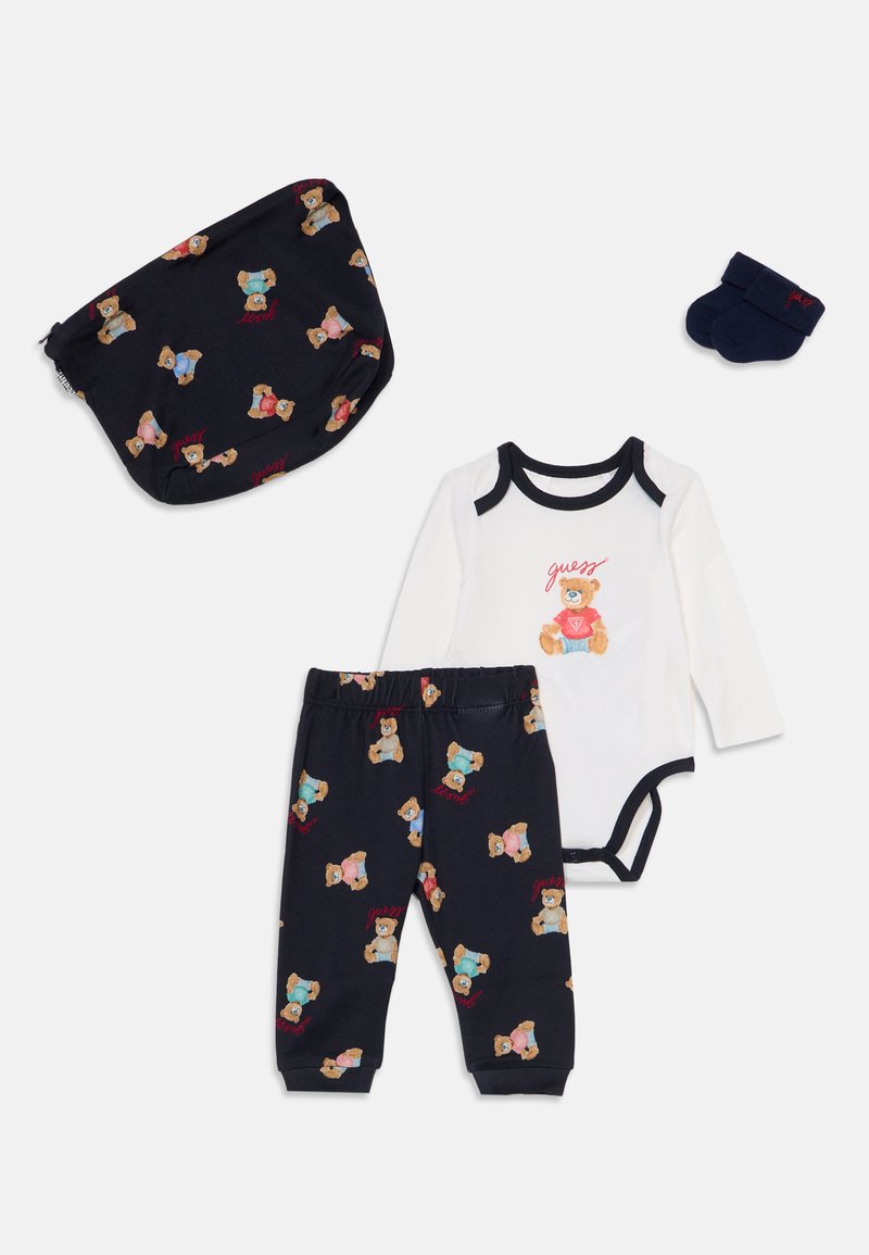 Ensemble pour bébé avec pantalon bleu marine à motif ours en peluche, bonnet et chaussettes assortis, et body blanc à manches longues avec motif ours en peluche.