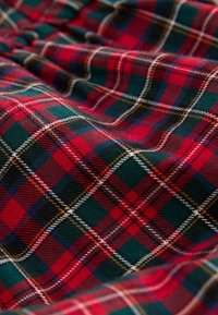 Rød og grøn tartan stof med et ternet mønster med hvide og gule accenter, som viser tekstur og dybde i vævningen.