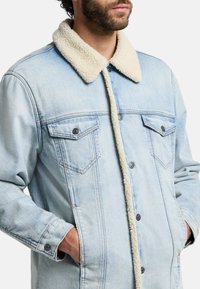 Ljusblå denimjacka med en krämfärgad faux shearling-krage, med knäppta bröstfickor och sidofickor.