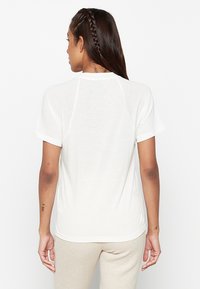 T-shirt bianca a maniche corte con scollatura rotonda e maniche raglan, caratterizzata da un orlo leggermente curvo e un piccolo logo sul retro.