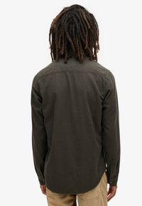 Lange mouwen shirt in donkergroene stof, met een rechte achterkant met stikdetails, manchetten met knopen en een afgeronde zoom.