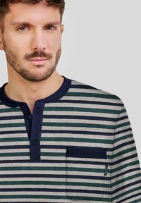 Camisa henley a rayas en gris, azul marino y verde. Presenta un cuello con botones y un bolsillo en el pecho con un acento en azul oscuro. Textura de tela suave.