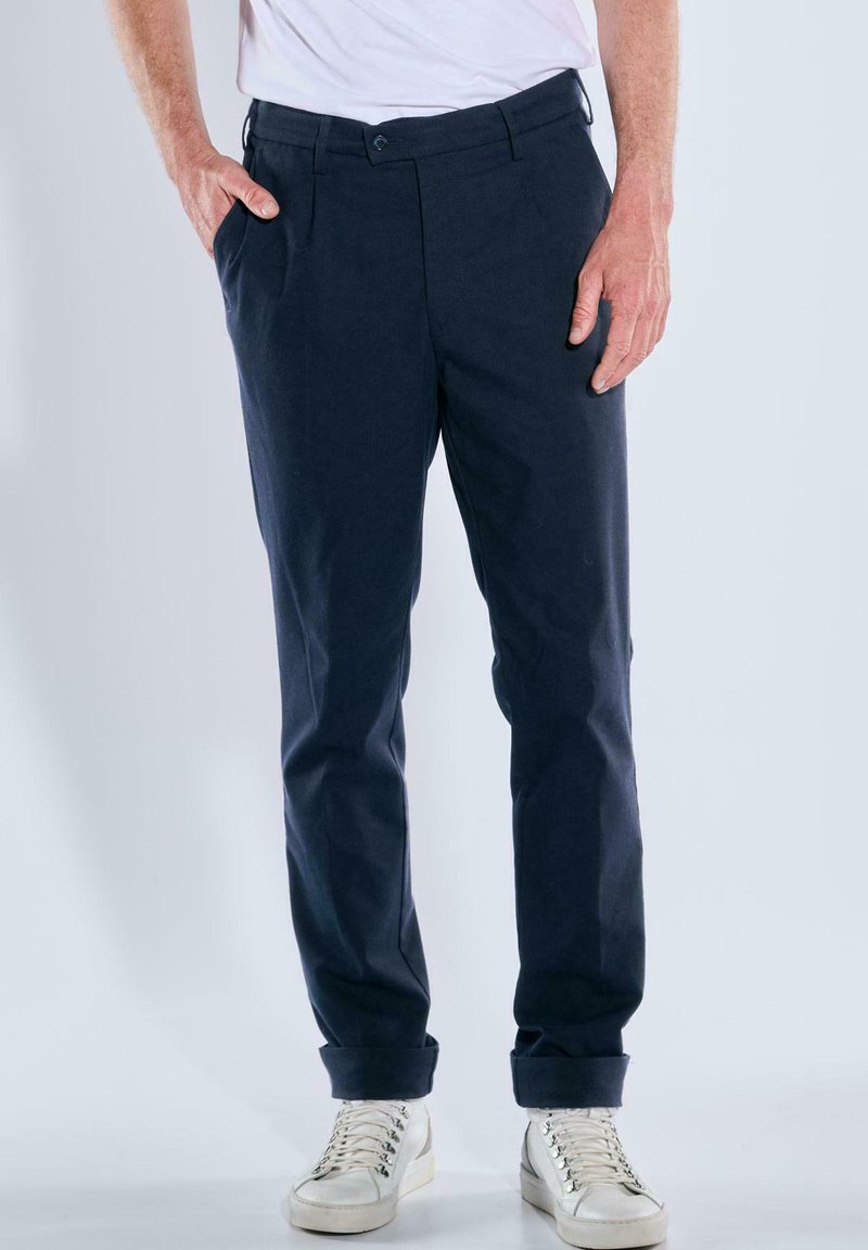Navy chinos with a tailored fit, featuring a smooth texture, front pleats, and side pockets, paired with white high-top sneakers.