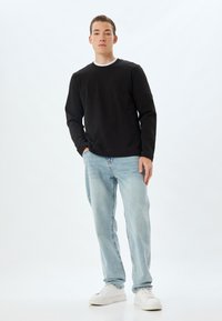 Sudadera negra con cuello redondo, combinada con jeans azul claro y zapatillas blancas. Diseño simple, de corte relajado, con mangas largas.