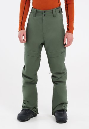 Un pantalon imperméable vert avec une taille haute, une fermeture à bouton, des poches cargo et une coupe décontractée aux chevilles, associé à des bottes noires.