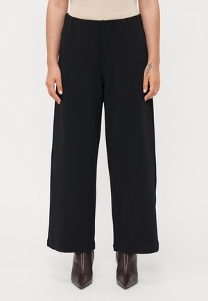 Zwarte wijde broek met een elastische tailleband, een gladde textuur en een losse pasvorm, gecombineerd met puntige bruine enkellaarsjes.