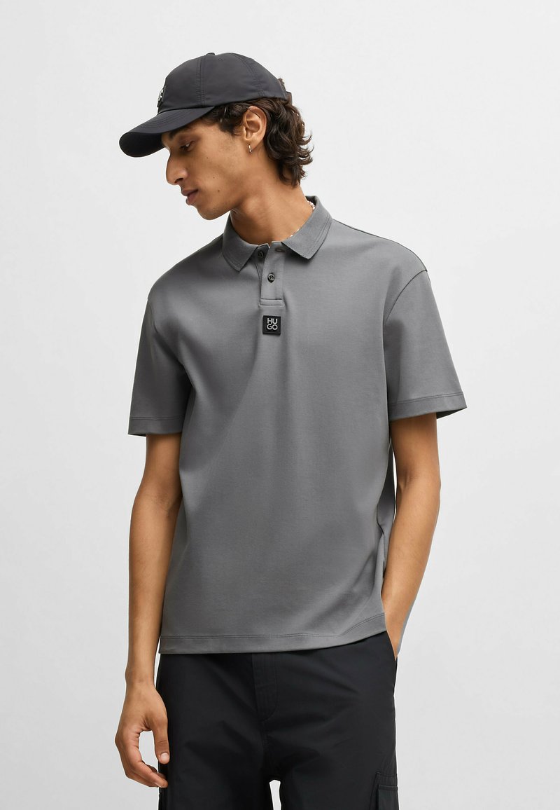 Grå polo shirt med korte ærmer, en klassisk knappet krave og et lille sort logo mærke. Accepteret af en matchende mørk kasket.