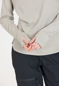 Lichtgrijze longsleeve shirt met duimopeningen, zachte textuur, ontspannen pasvorm, gecombineerd met zwarte broek met een ritszak en een gladde afwerking.