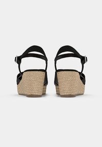 Sandales compensées espadrilles noires avec un talon en paille texturé et une bride de cheville à boucle. Matière supérieure lisse avec une silhouette incurvée.