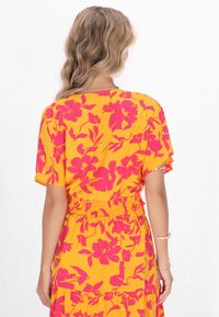 Gelbes Blumenkleid mit auffälligen pinken Blumenmustern, kurzen Ärmeln und einer gerafften Taille mit gestuften Lagen.