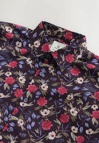 Bloemmotief shirt met een donkere paarse achtergrond en roze en witte bloemen. Het heeft een standaard kraag en drie knopen aan de voorkant.