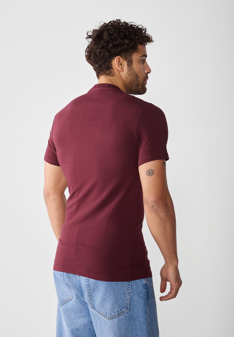 Bordeaux kortemouwen t-shirt van zacht materiaal, met een getailleerd ontwerp en een ronde halslijn, gedragen met lichtblauwe denim shorts.