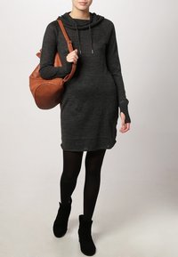 Robe pull en charbon avec un col chauve-souris, des manches longues et des fentes sur les côtés. Assortie à un sac à épaule marron et des bottines noires.