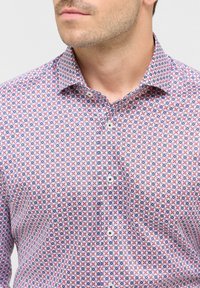Hemd aus Baumwollstoff mit einem geometrischen Muster in Rot, Blau und Weiß, mit einem spitzen Kragen und weißen Knöpfen.