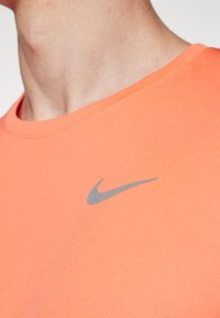 Orange atletisk skjorte med en tekstureret finish og en rund halsudskæring. Har et gråt Nike swoosh logo på venstre bryst.