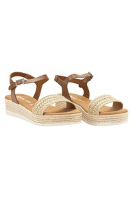 Sandalias de imitación de cuero marrón con correas de paja trenzadas, hebilla ajustable en el tobillo y suela de cuña, con una plataforma texturizada de color beige y suela blanca.