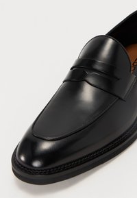 Mocasin din piele neagră cu finisaj neted și lucios, o bandă decorativă ridicată pe partea superioară și un design cu vârf rotund; toc plat.