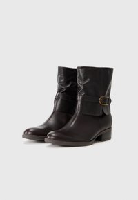 Par de botas de cuero marrón oscuro hasta la mitad de la pantorrilla con tacones bajos y correas de hebilla en los laterales sobre un fondo neutro.