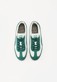 Grüne Wildleder- und weiße Leder-Sneaker mit einem gemusterten Innenfutter, flachen Schnürsenkeln und einer Gummiaußensohle. Mit einem Puma-Logo auf der Zunge.