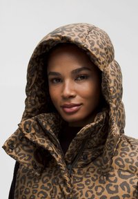 Polo i brunt med sort leopardprint. Har høj krave, lynlås foran og skjulte knapper. Glansfuld overflade og tekstureret stof.