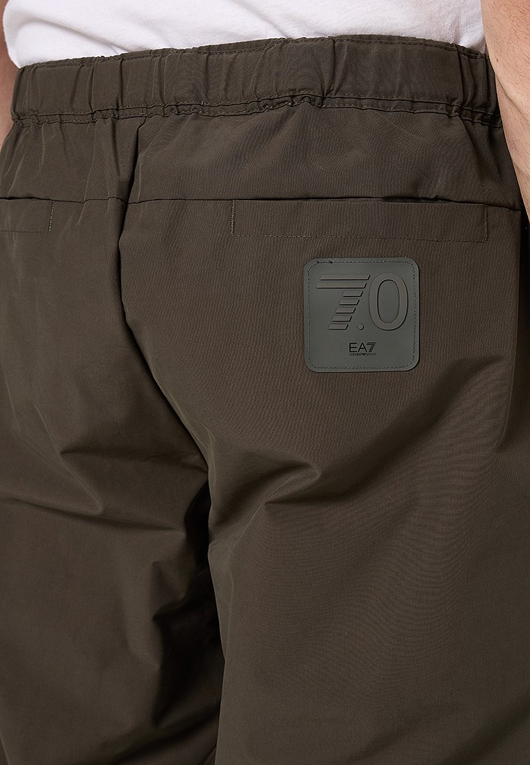 Pantaloni verde oliva scuro con una finitura testurizzata, caratterizzati da una vita elastica e una toppa quadrata con il marchio sulla tasca posteriore.