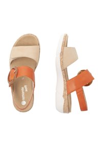 Sandales beige et orange avec un accent circulaire, en matériaux de daim et de cuir lisse, semelle texturée et design de sangle réglable.