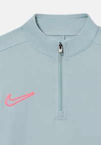 Sweatshirt bleu clair à zip quart, fabriqué en tissu lisse, avec un logo Nike brodé rose sur la poitrine gauche et un col zippé.