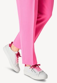 Sneaker bianchi con accenti e lacci rosa, abbinati a pantaloni rosa a gamba stretta. I sneakers hanno una superficie testurizzata e un dettaglio con zip laterale.