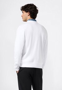 Sudadera blanca con cuello redondo y puños elásticos, combinada con pantalones negros. Presenta una textura suave y un ajuste clásico.