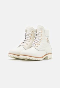 Bottines blanches en cuir avec quincaillerie dorée, surface texturée, épaisse semelle extérieure blanche et laçage à l'avant. Présente des accents argentés minimaux.